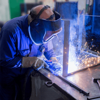 Photo d'un homme travaillant chez MSJ Industrie. Il porte un masque car il fait de la soudage. Des étincelles jaillissent.