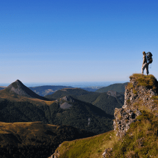 Randonneur sur une falaise admirant les montagnes auvergnates au loin