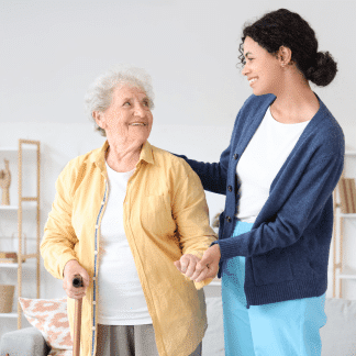 Aide à domicile aidant une femme âgée, toutes les deux souriantes et complices.